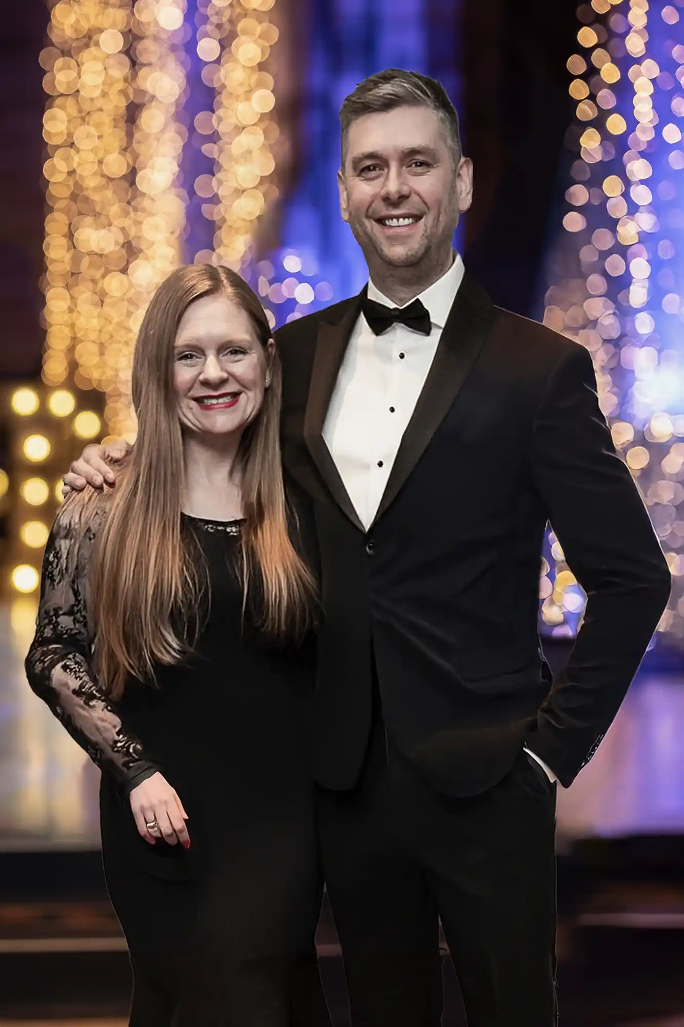 Claire and Jonathon Fowler dressed in formal attire stand in front of a background of decorative lights at Mansfield Traquair in Edinburgh.