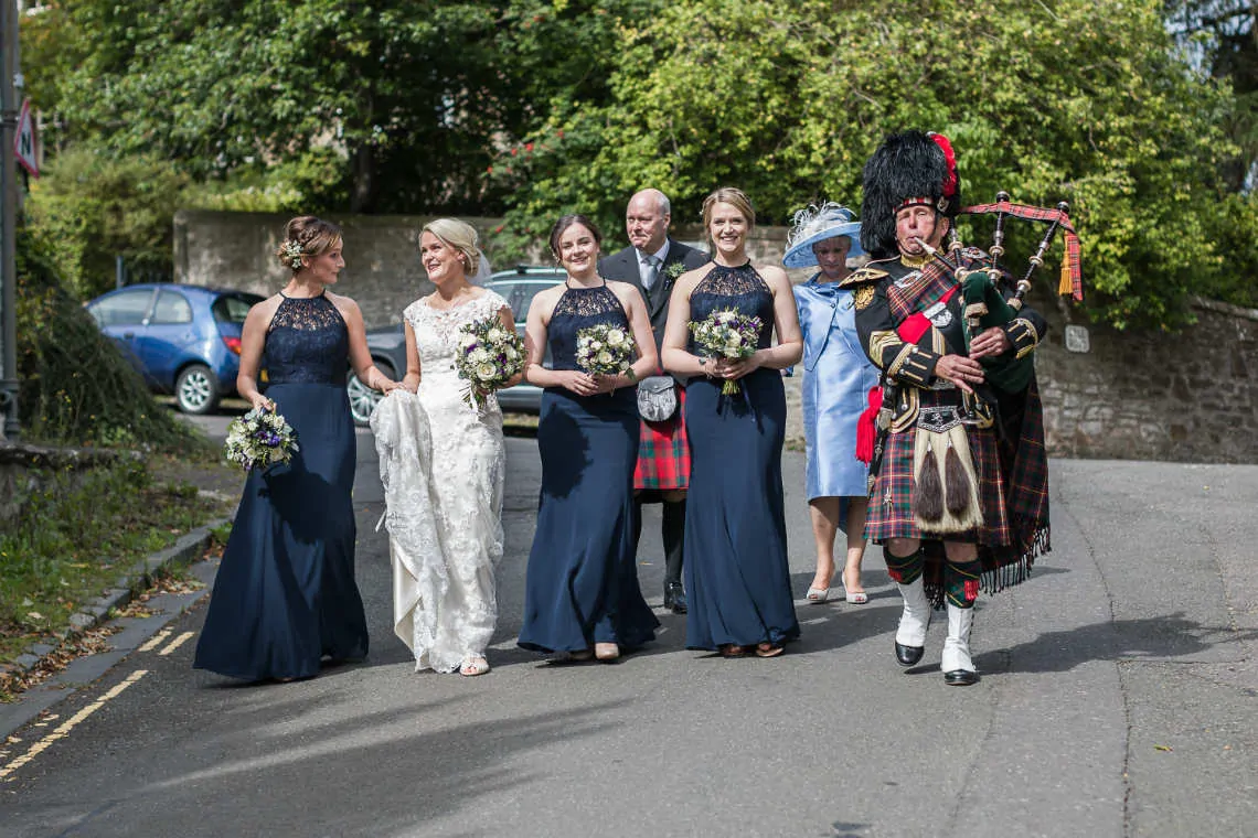 Bridal party and piper walking down the road to the church