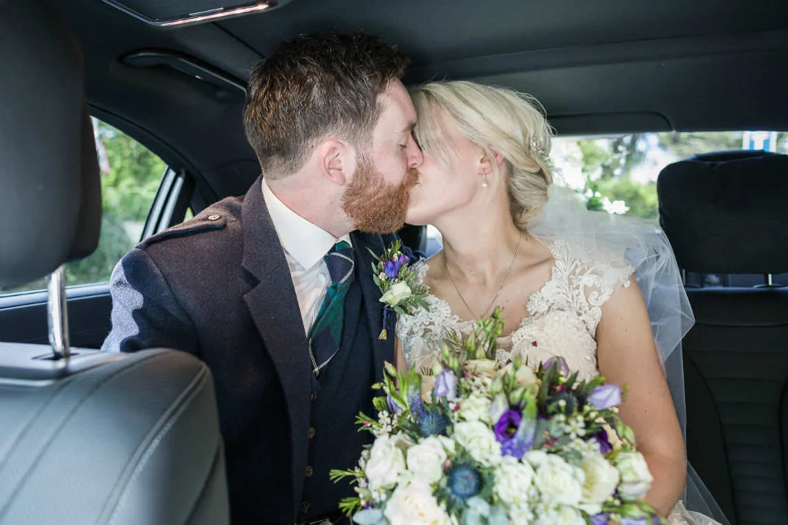 Bride and groom kiss in car