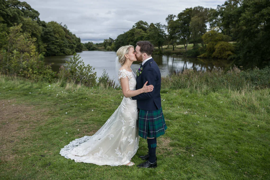 Newlyweds kiss in front of pond at Dalmahoy Hotel