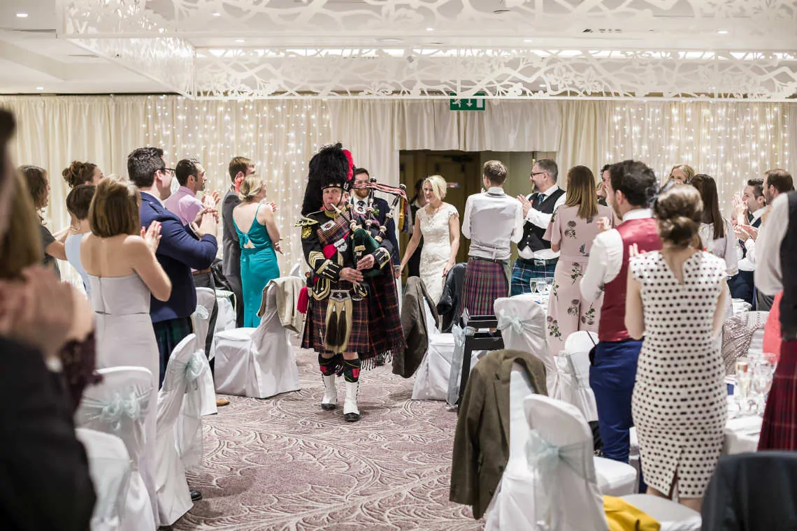 Newlyweds are piped into reception with guests standing and clapping