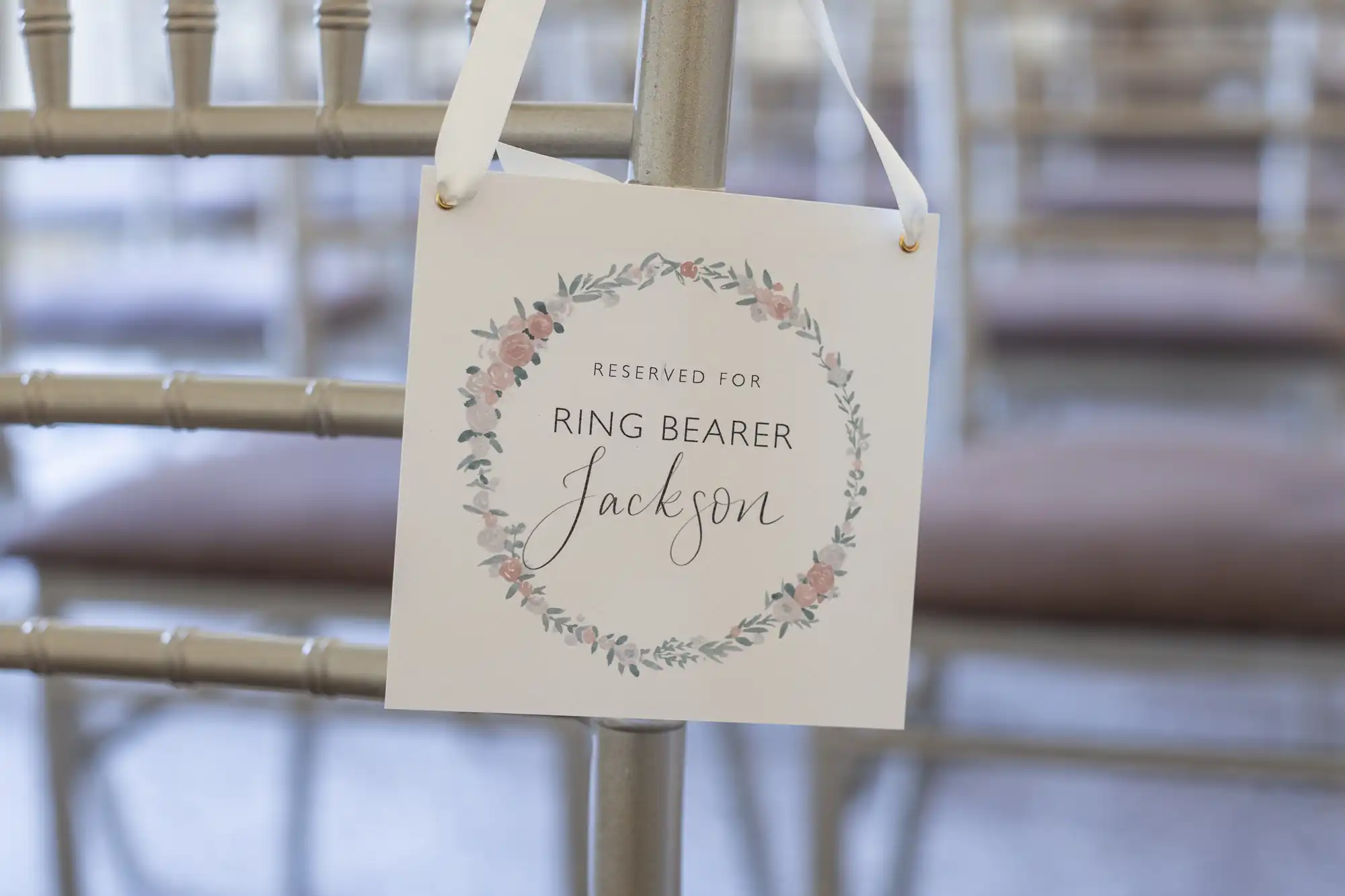 A sign on a chair reads "Reserved for Ring Bearer Jackson," decorated with a floral wreath design.