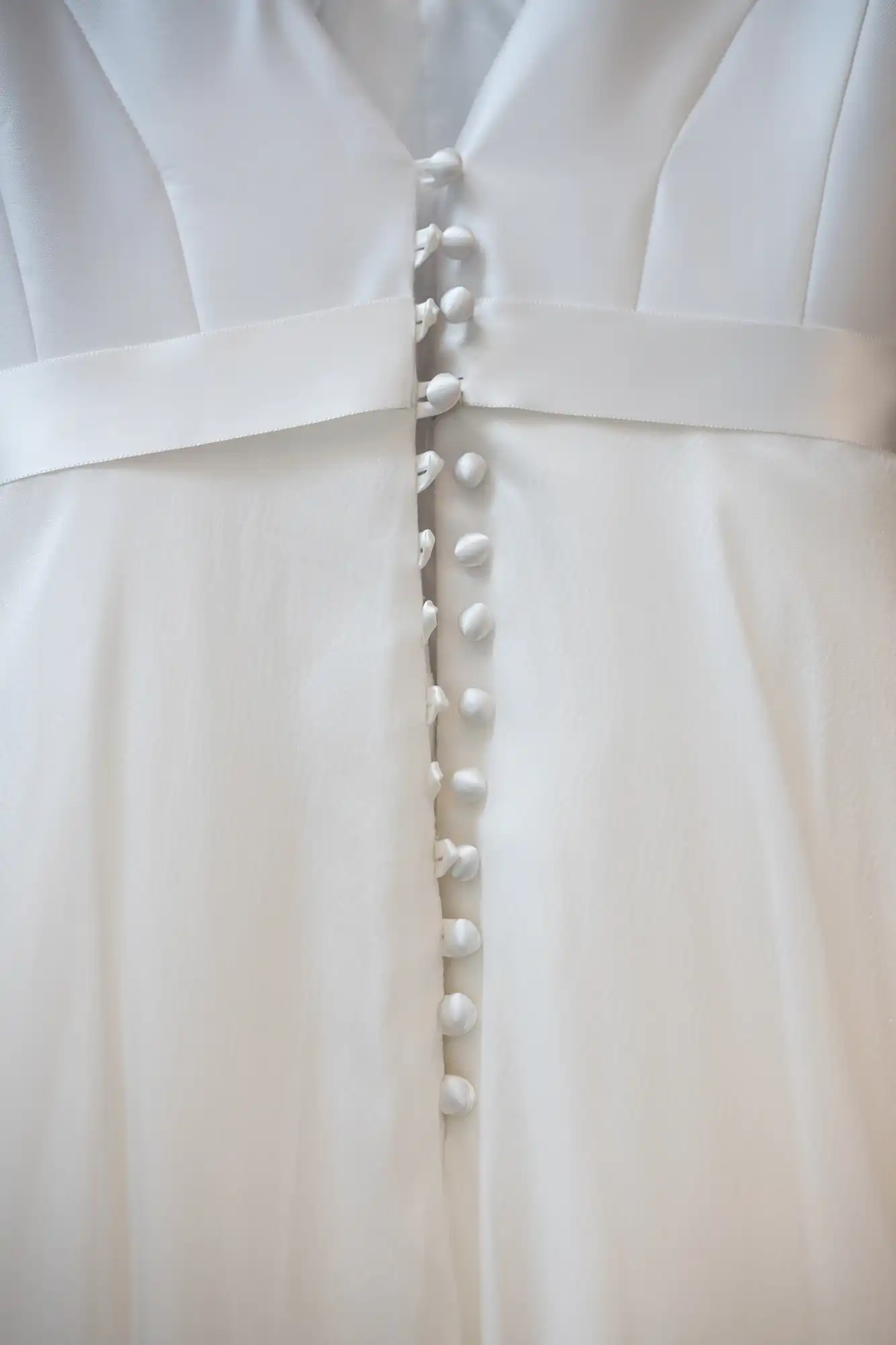 Close-up image of a white dress showing a row of fabric-covered buttons down the front.