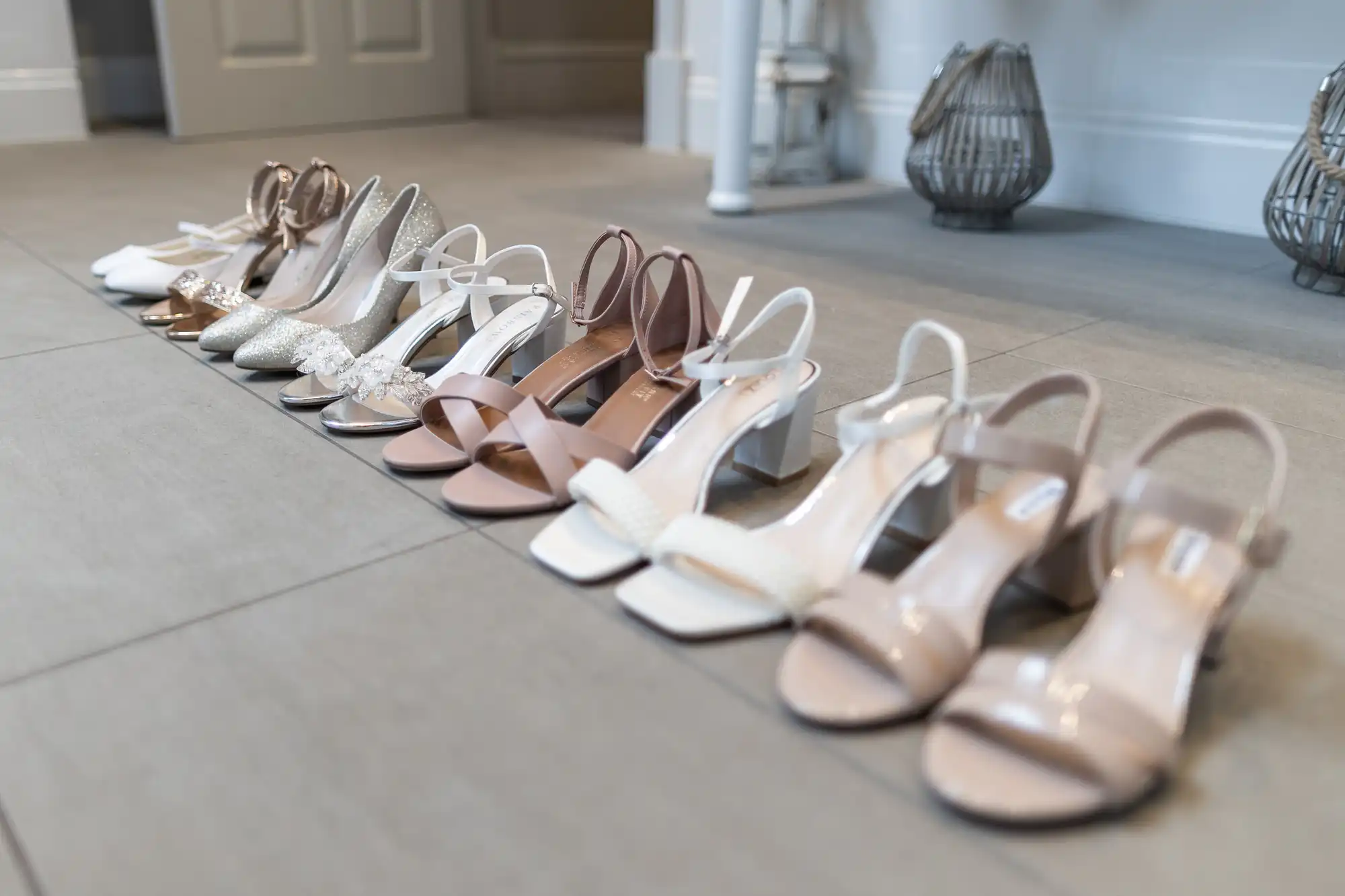 A row of women's high-heeled shoes in various neutral colors lined up on a wooden floor indoors.