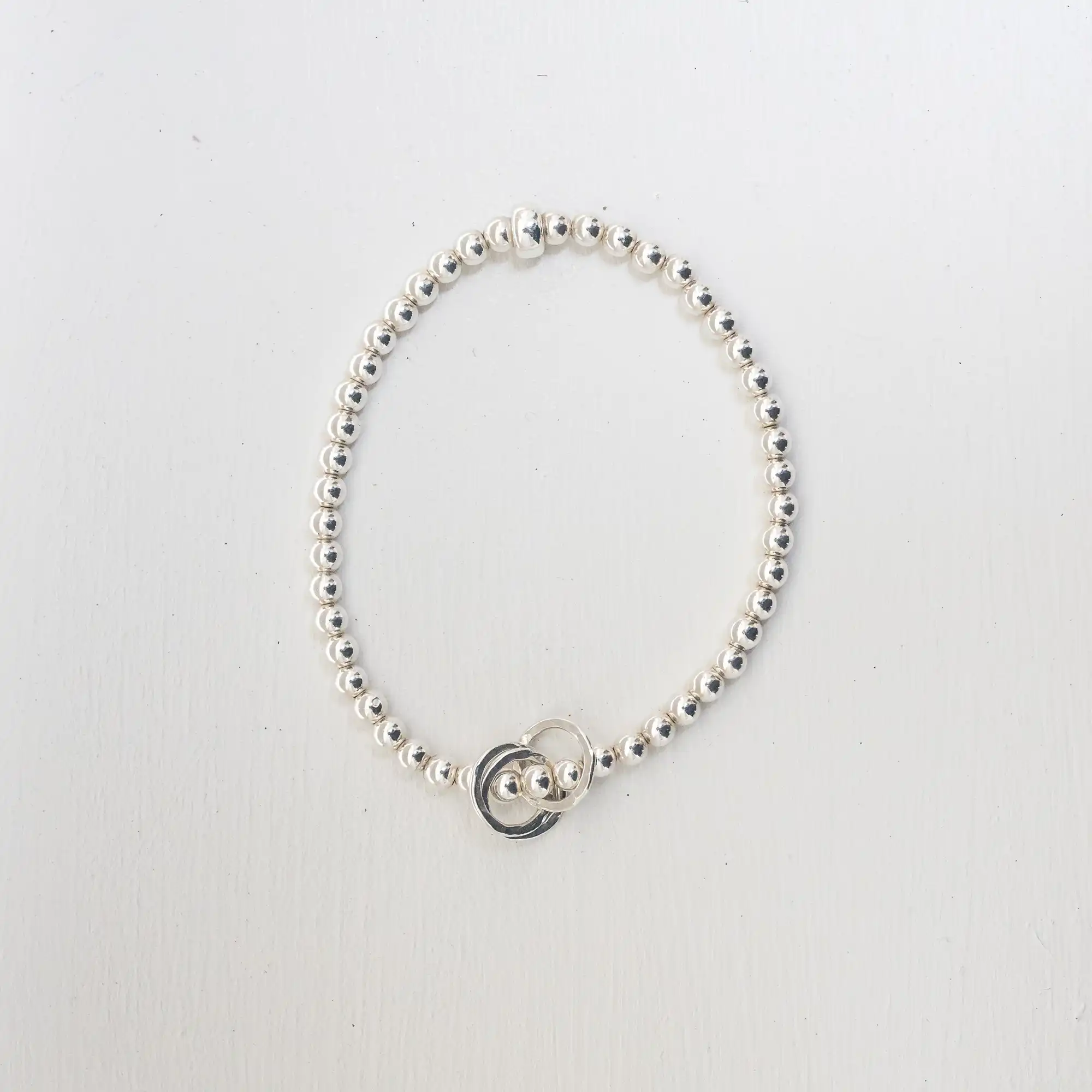 A silver beaded bracelet with a small silver loop charm placed on a white surface.