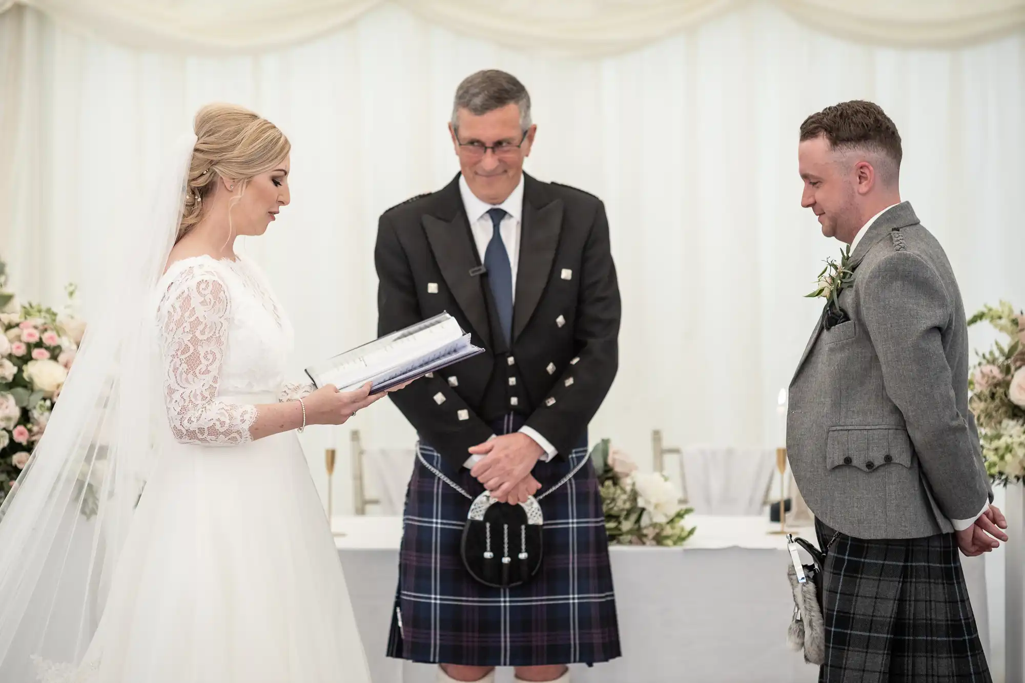 A bride and groom stand facing each other during their wedding ceremony, with an officiant in traditional attire standing between them.