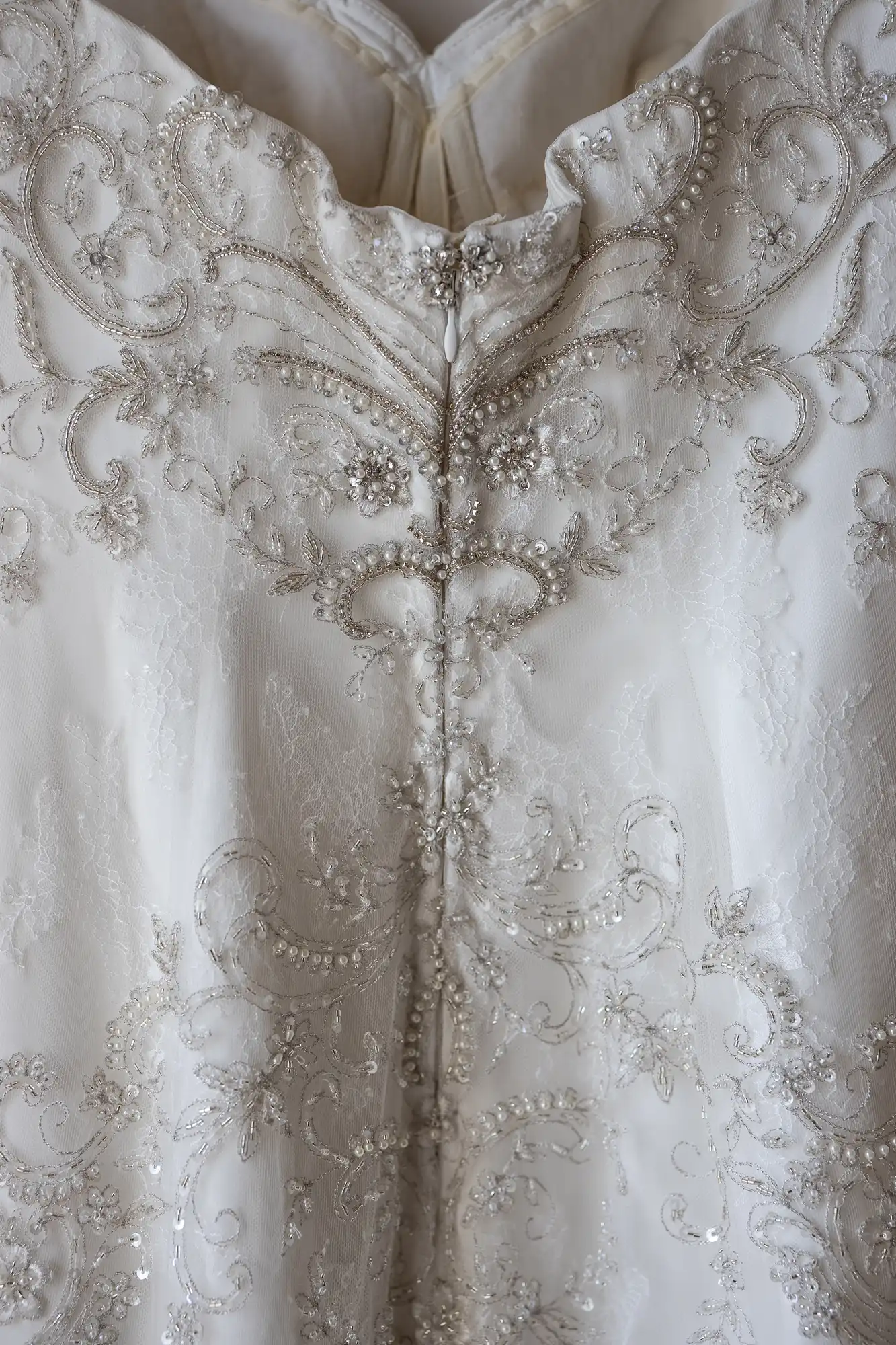 Close-up view of an ornate wedding gown featuring intricate embroidery, beadwork, and lace detailing.