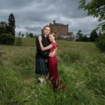 newlyweds embrace as they stand in the meadow in front of the castle