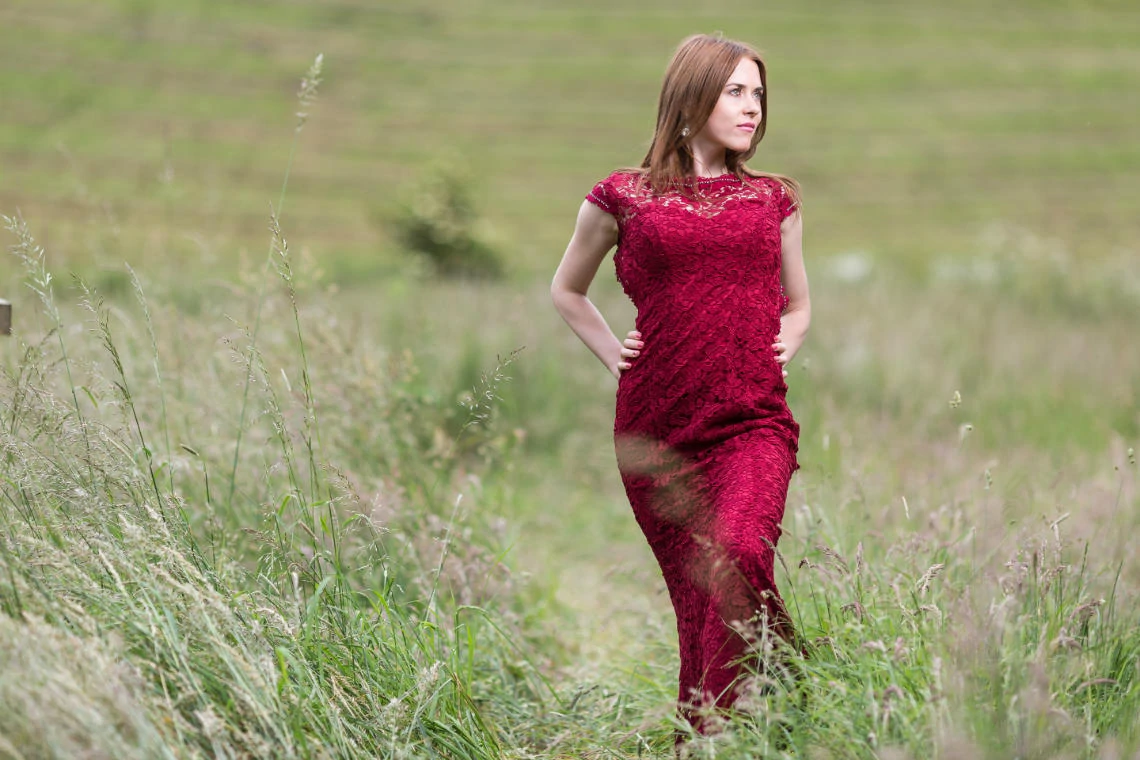 bride wearing red lace dress standing in the meadow beneath the castle