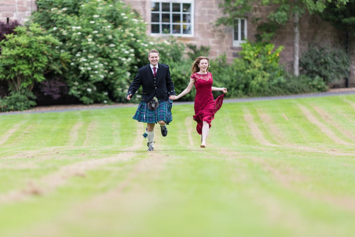 newlyweds laughing holding hands as they run across the castle lawn