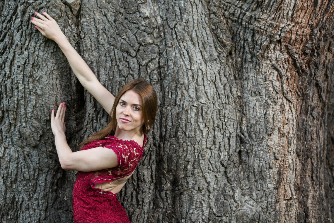 bride wearing a red lace dress poses in front of the large tree on the castle lawn