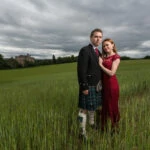 bride and groom standing in the field with the castle in the background