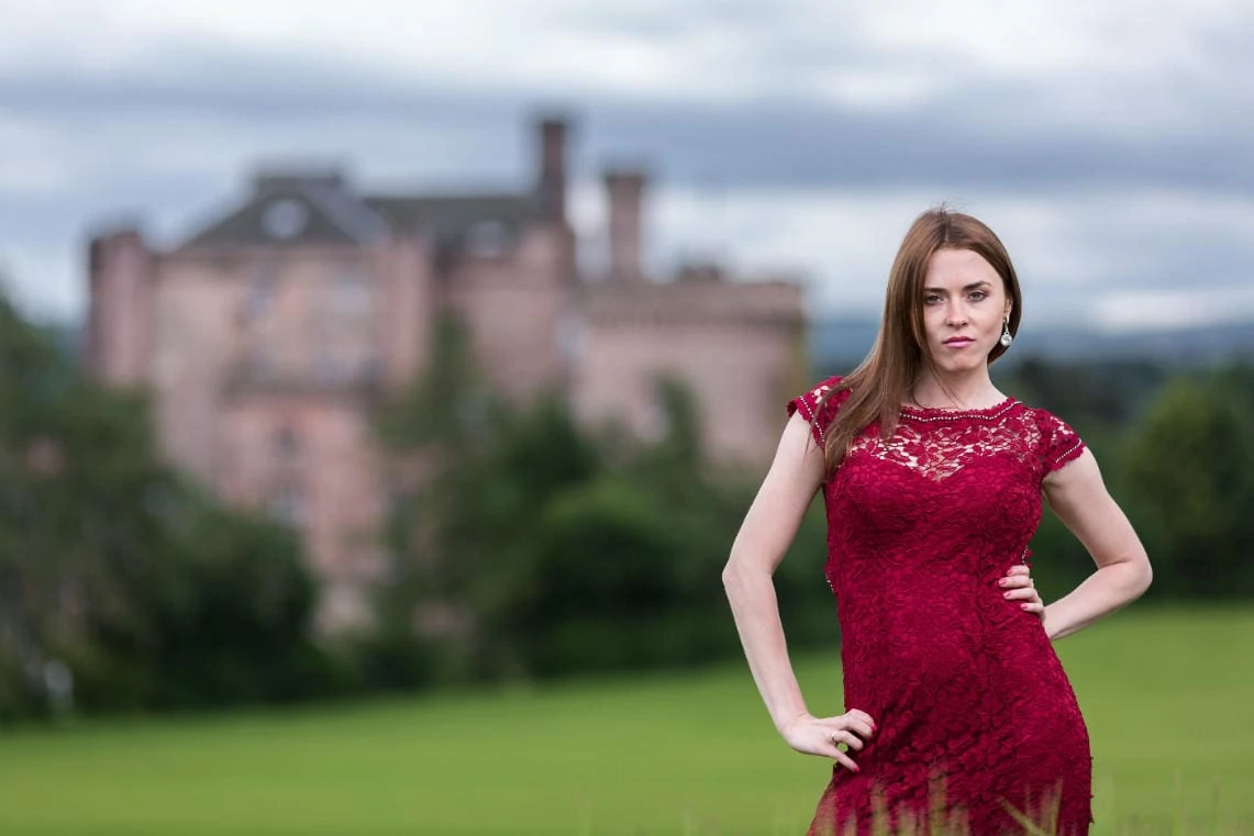 bride wearing a red lace dress standing in the field with the castle in the background