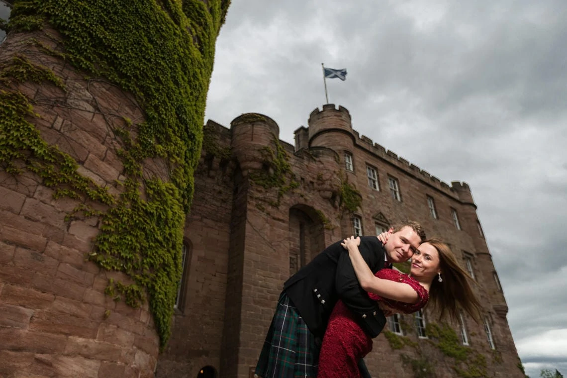 newlyweds embrace at the entrance to the castle with the Scottish flag flying high