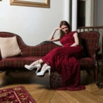 bride wearing a red lace dress and white heels relaxes on a chaise longue in the reception area