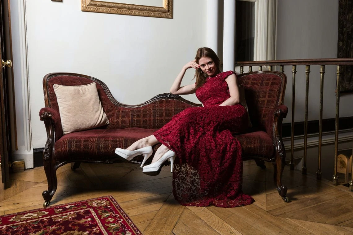 bride wearing a red lace dress and white heels relaxes on a chaise longue in the reception area