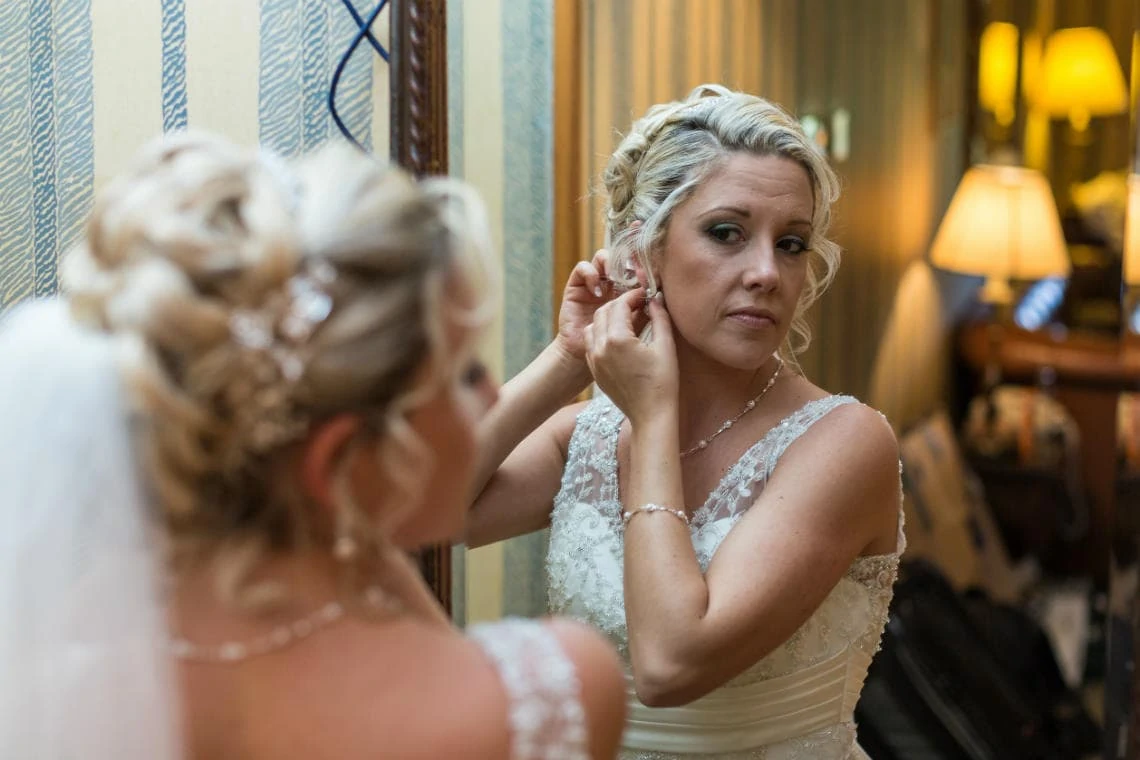 bride putting in her earrings in front of a mirror in the bedroom