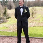 groom wearing black tuxedo and bow tie standing outside the castle