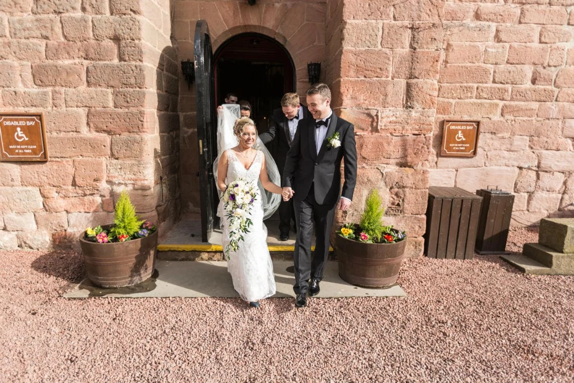 newlyweds holding hands as they exit the castle into the sunshine