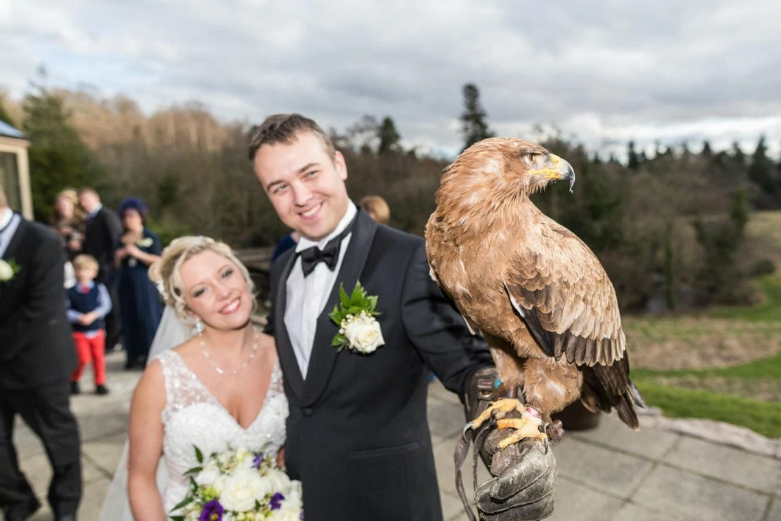 groom holding an eagle on the castle patio as his bride watches