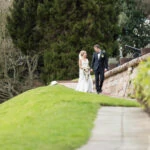 newlyweds walking down the path towards the arched bridge