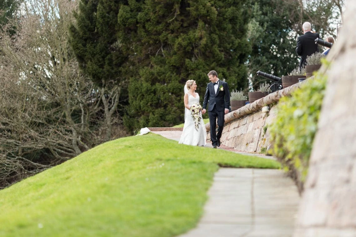 newlyweds walking down the path towards the arched bridge