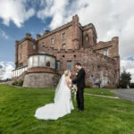 newlyweds standing on the grass with the castle in the background