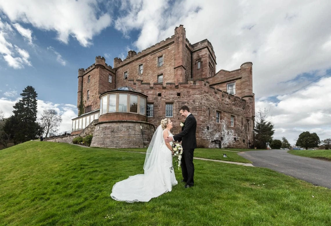 newlyweds standing on the grass with the castle in the background