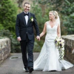 newlyweds smiling and holding hands as they walking across the bridge