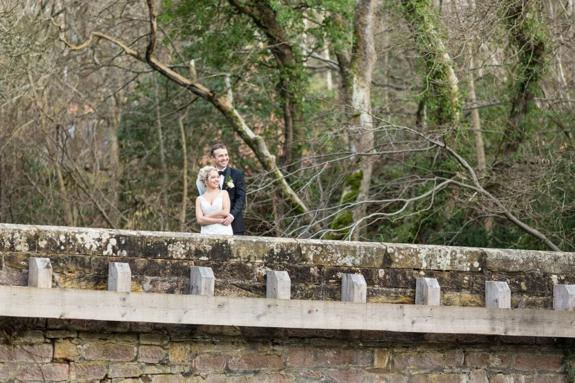 newlyweds embrace and smile as they stand on the arched bridge