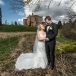 newlyweds embrace and look at each other as they stand in the meadow in front of the castle
