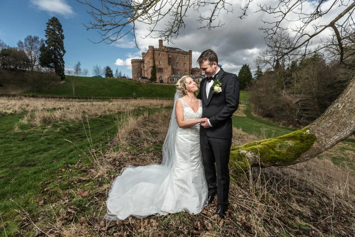 newlyweds embrace and look at each other as they stand in the meadow in front of the castle
