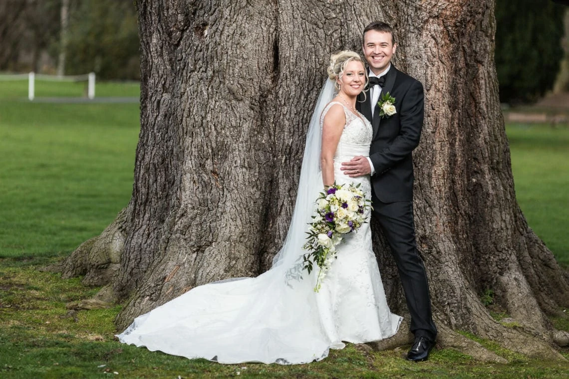 newlyweds embrace in front of an old tree on the lawn of the castle