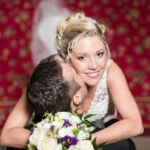 groom kisses bride's neck at the bottom of the castle staircase