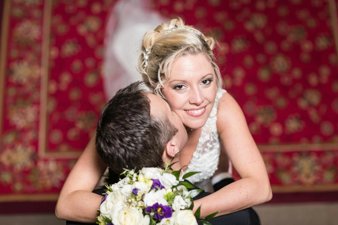 groom kisses bride's neck at the bottom of the castle staircase