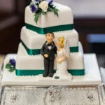 white wedding cake with green ribbons and miniature newlyweds
