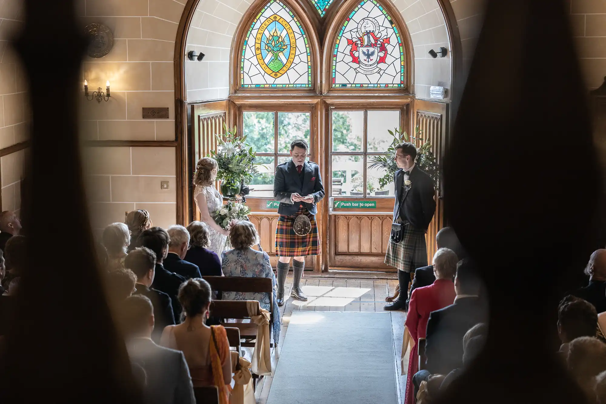 A wedding ceremony in a church features a bride, groom, and officiant standing at the altar. The congregation is seated, and the scene is framed by stained-glass windows and wooden pews.