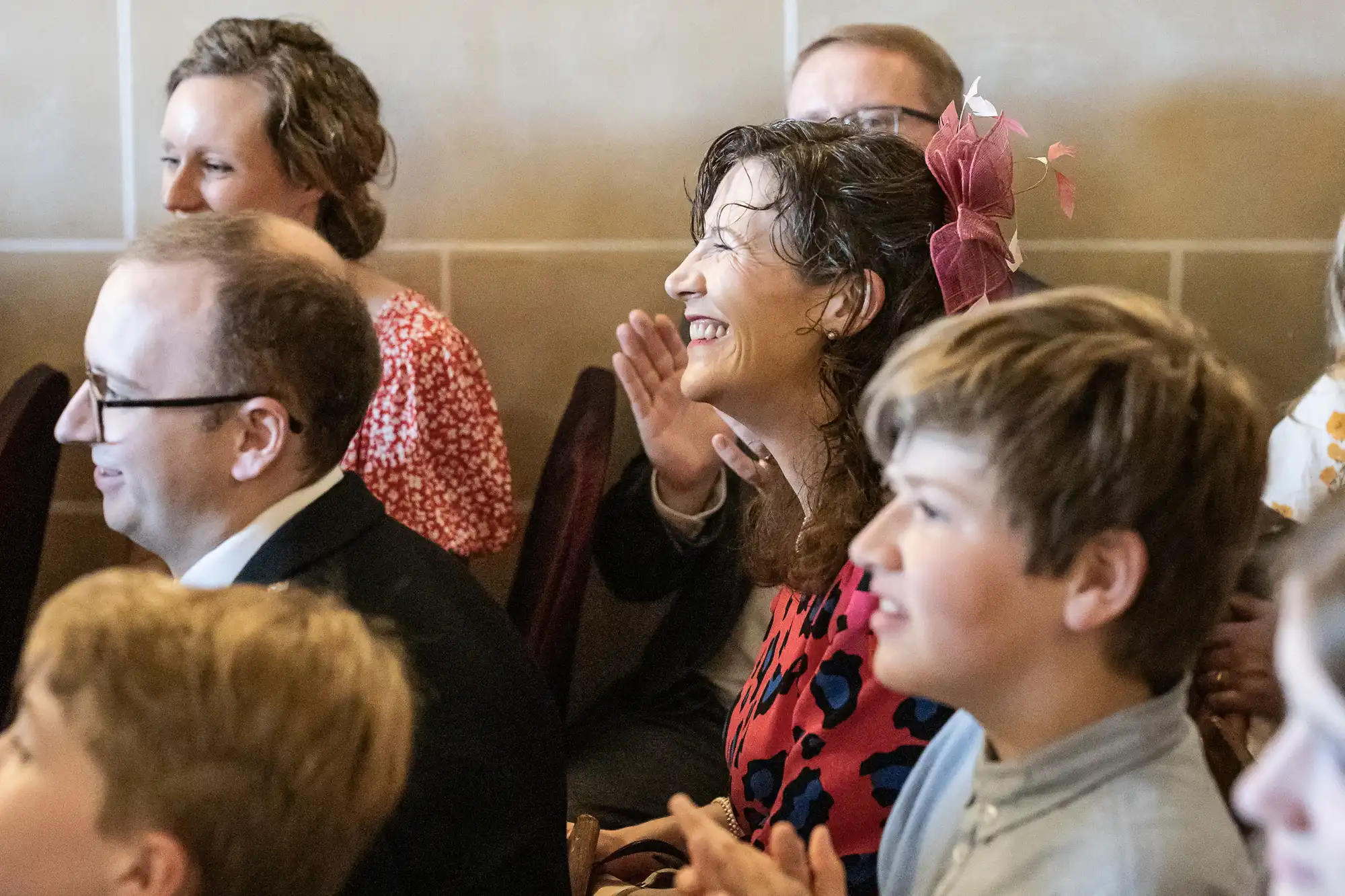 A group of people seated and smiling, with some clapping, in what appears to be an indoor setting.