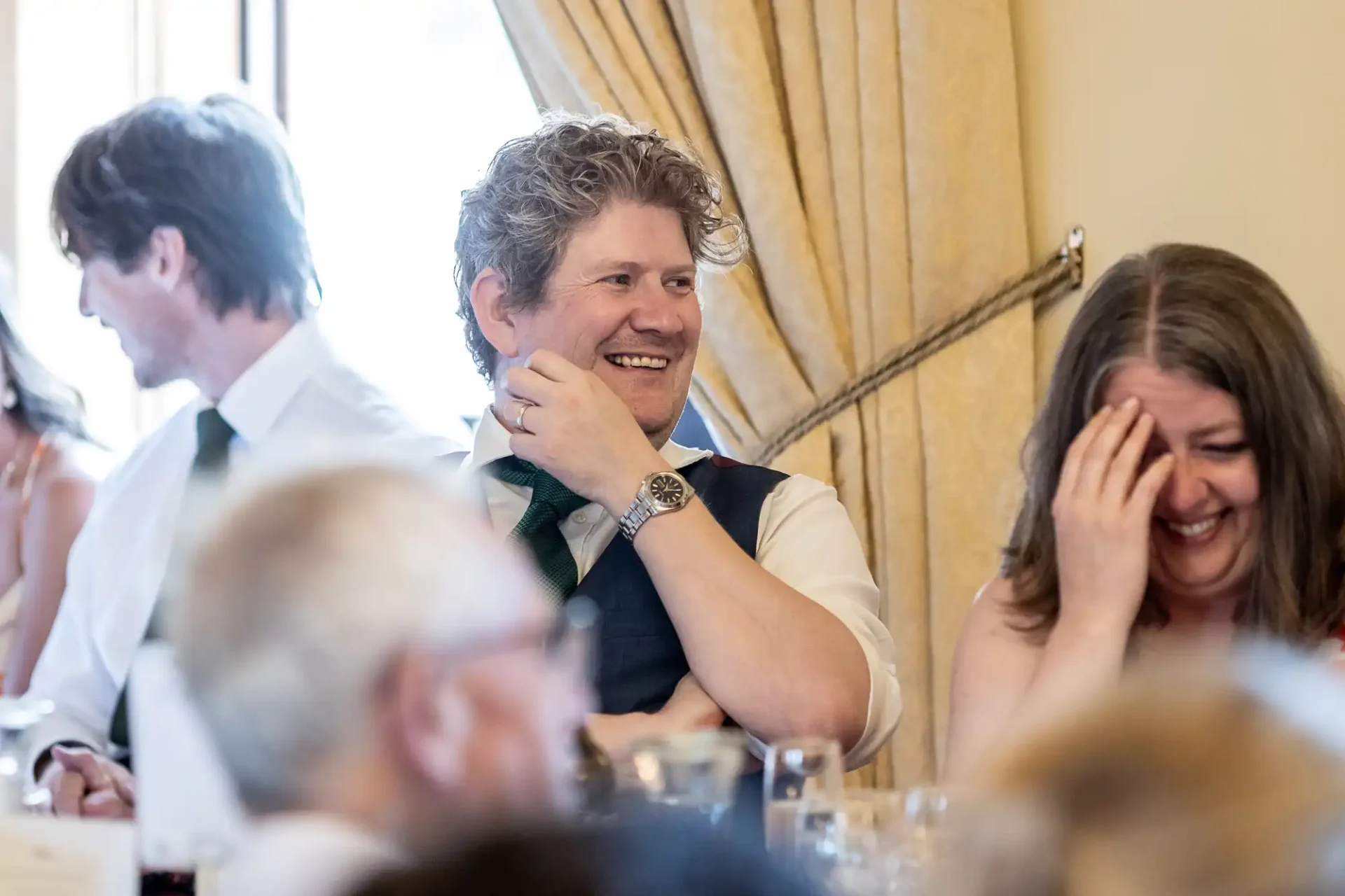 Man smiling and woman laughing while seated at a formal event, with others around them.