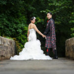 bride and groom holding hands as they walk across the arched bridge