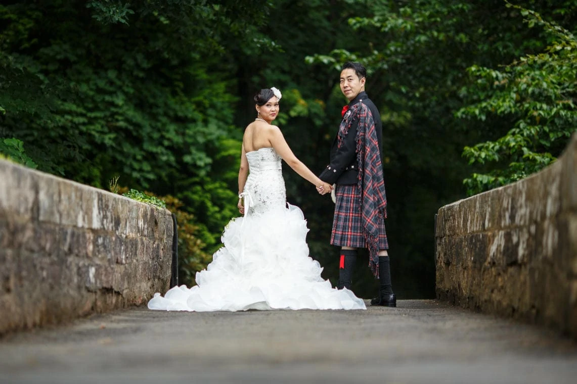 bride and groom holding hands as they walk across the arched bridge