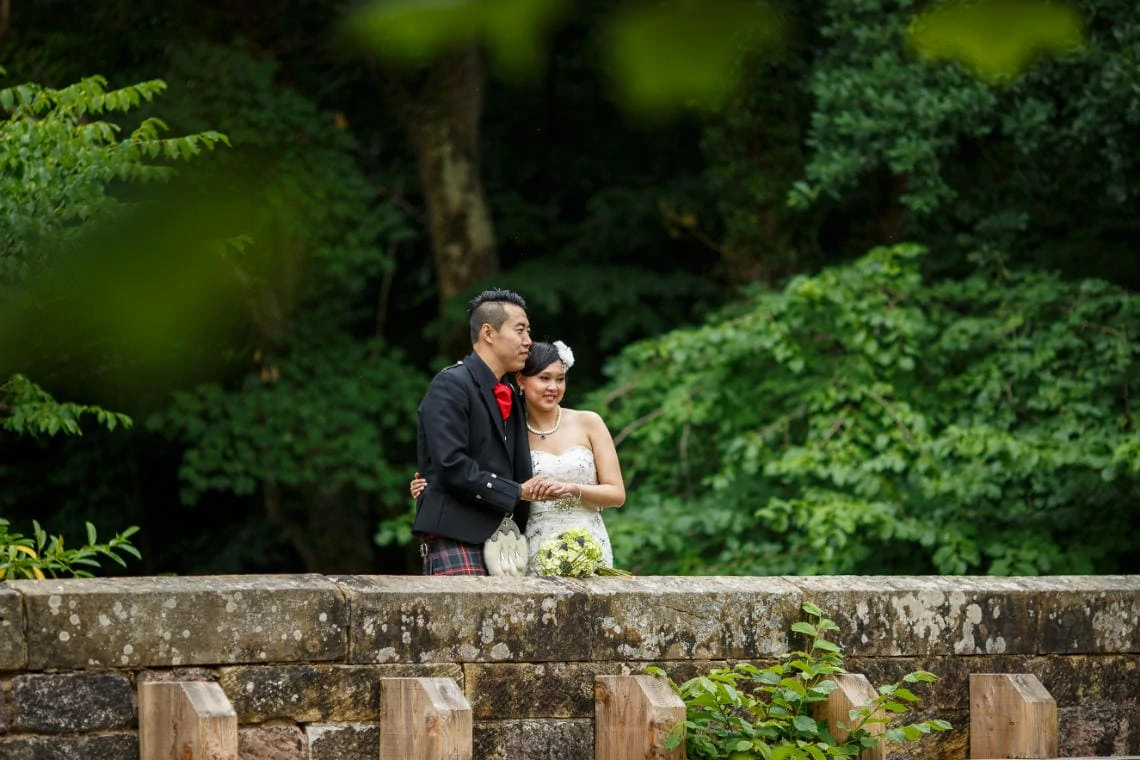 newlyweds embrace as they look out from the arched bridge