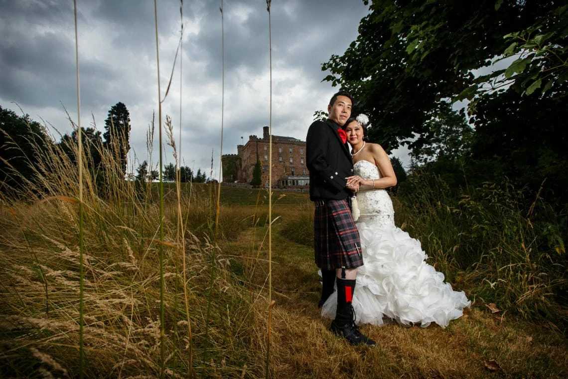newlyweds embrace in the meadow with the castle in the background