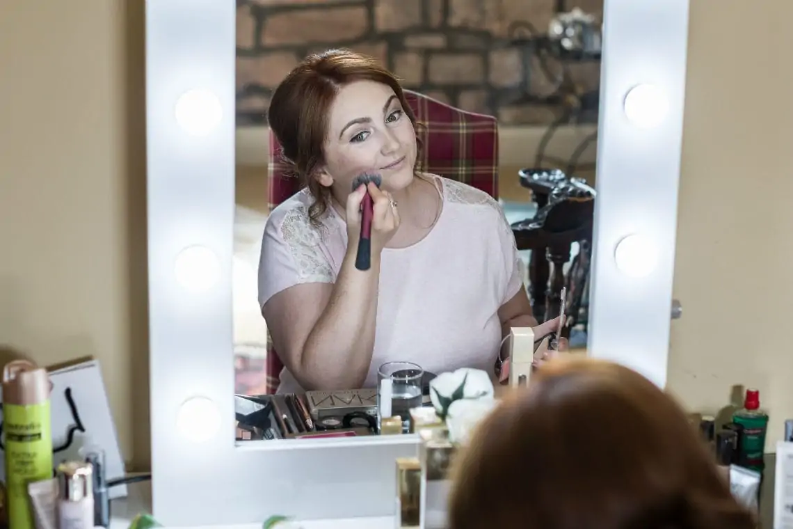 Bridesmaid doing her makeup in front of a mirror.