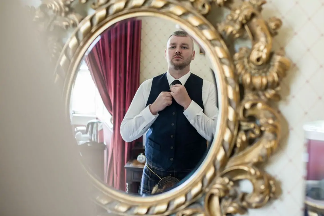 Groom looking into a mirror and adjusting his tie.