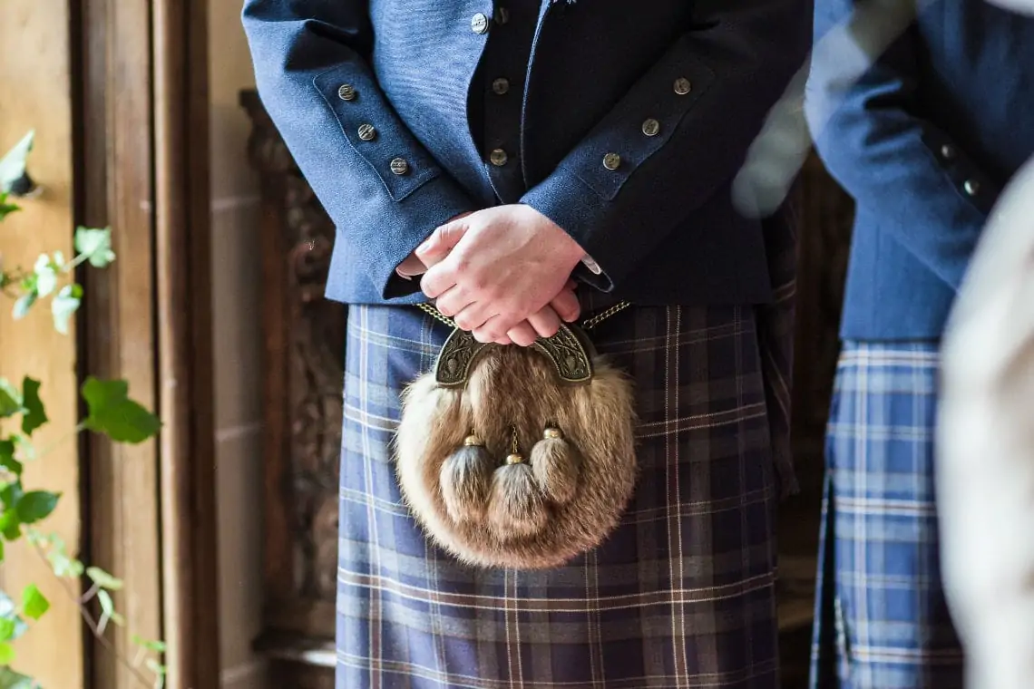 Close up of groom's crossed hands and kilt sporran.