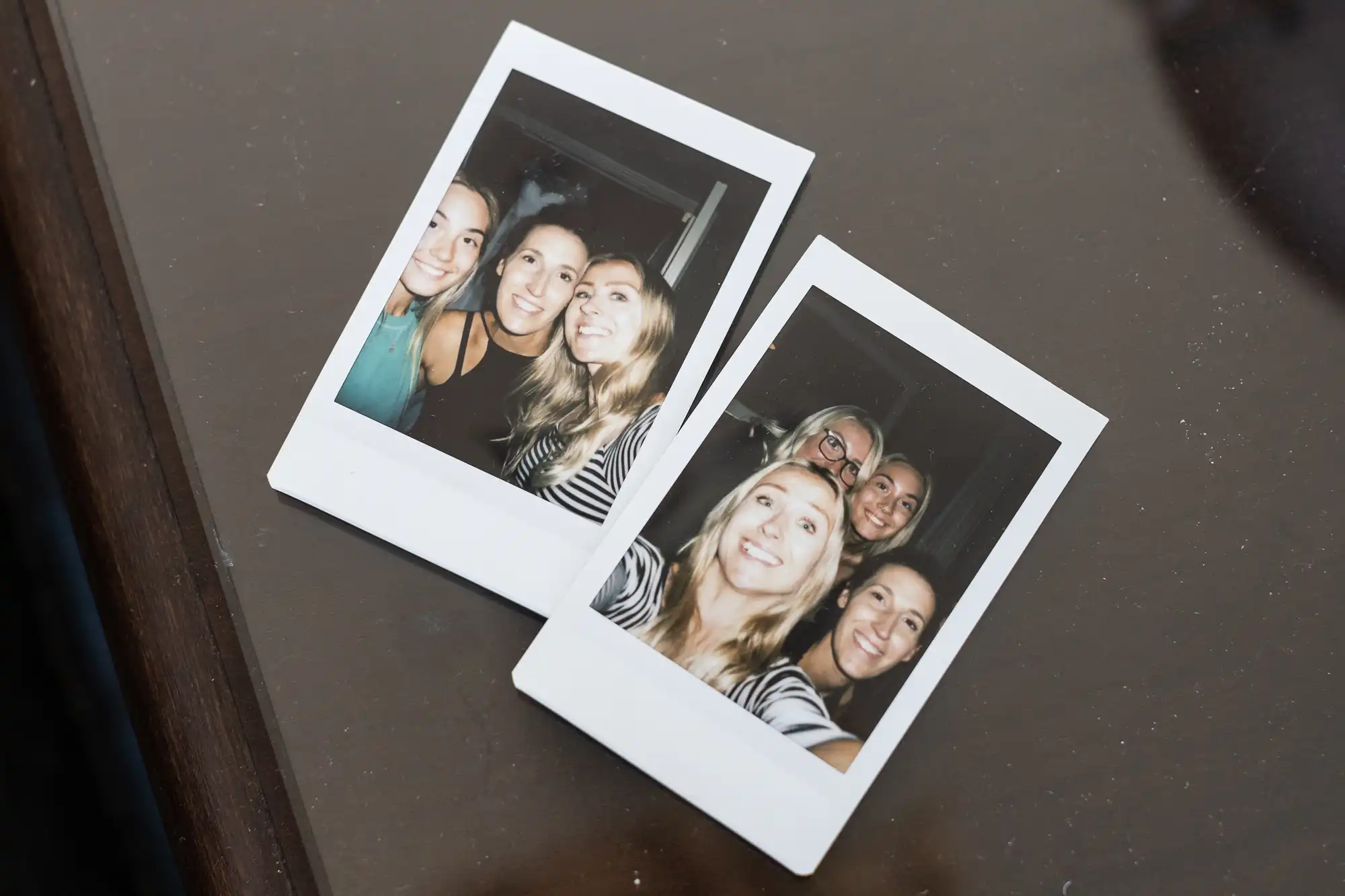 Two Polaroid photos on a table, each showing a group of four smiling people posing closely together.