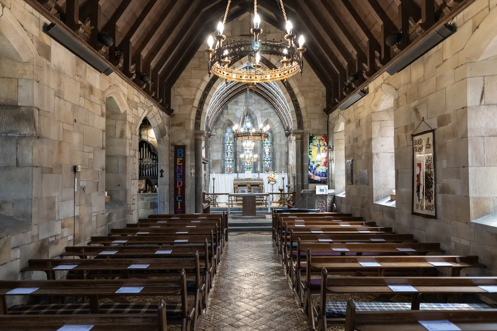 Interior of a small chapel with wooden pews, a chandelier, and an altar at the front. Stained glass windows and stone walls create a traditional church atmosphere.