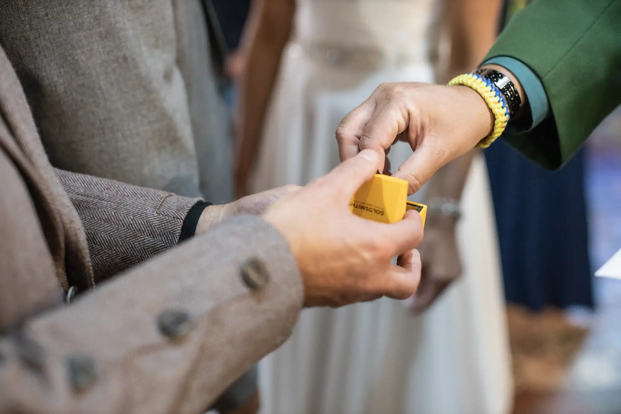 One person is handing over a small yellow box to another. Both individuals are dressed in formal clothing.