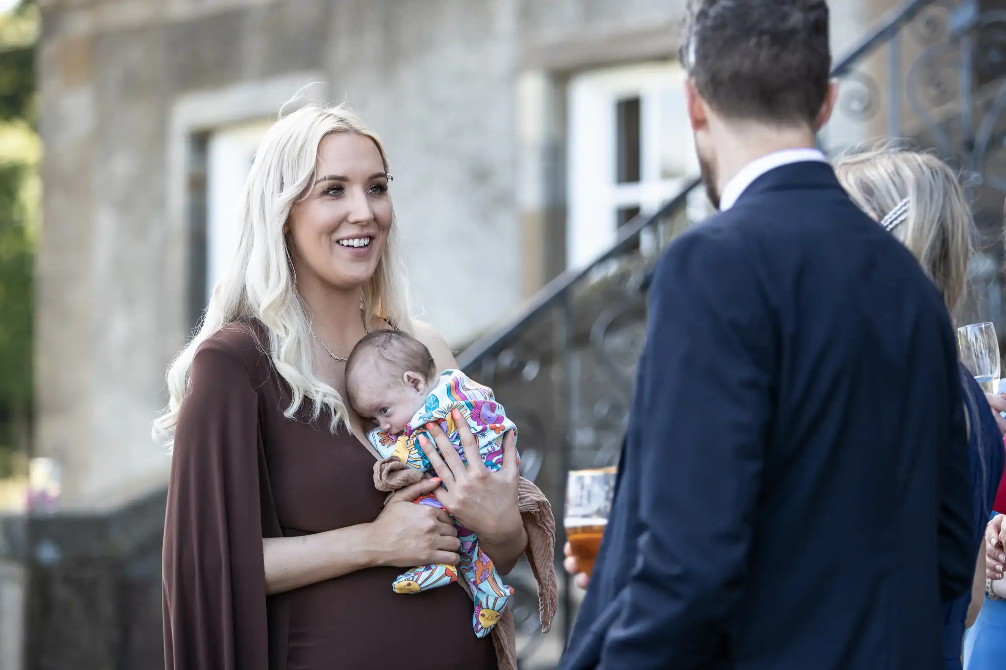 A woman holding a baby is talking to a man and two other people at an outdoor event.